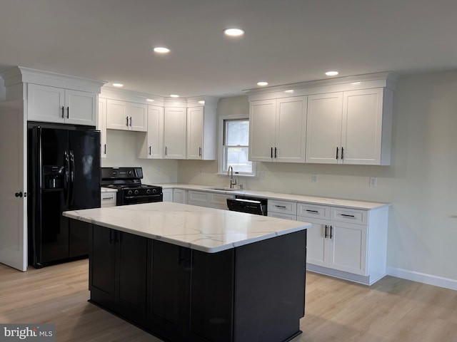 kitchen featuring light stone countertops, black appliances, sink, a kitchen island, and white cabinetry