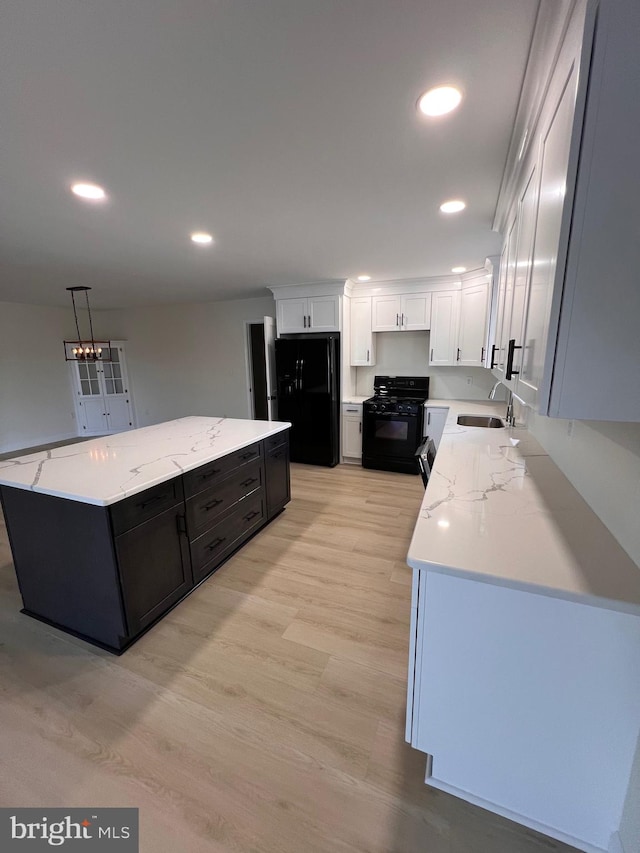 kitchen featuring black appliances, a kitchen island, hanging light fixtures, white cabinets, and light hardwood / wood-style flooring