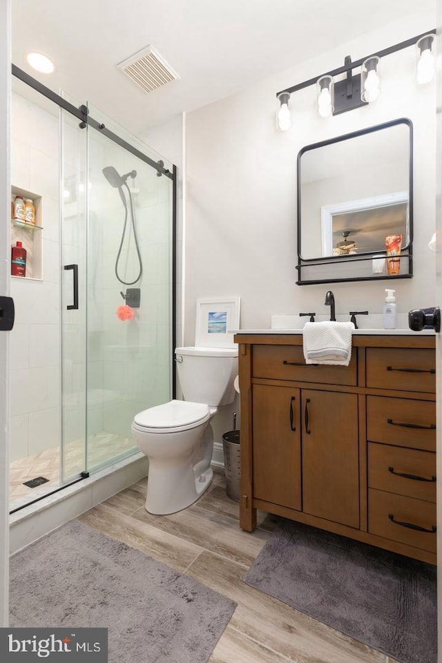 bathroom with vanity, hardwood / wood-style flooring, ceiling fan, toilet, and a shower with shower door