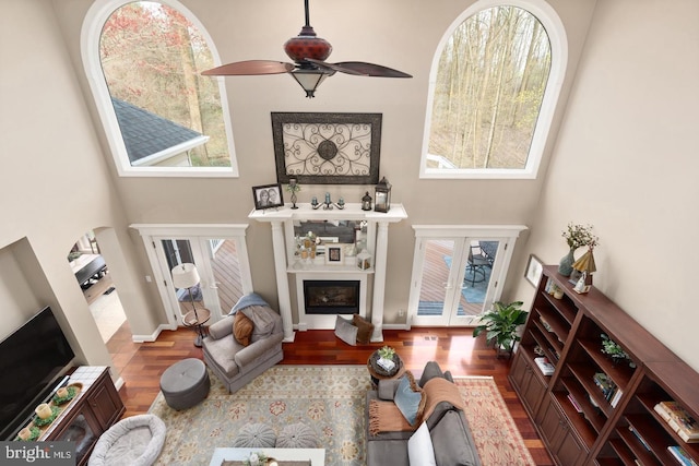 living room with ceiling fan, french doors, a towering ceiling, and hardwood / wood-style flooring