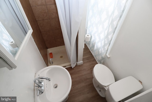 bathroom with toilet, a sink, a stall shower, and wood finished floors