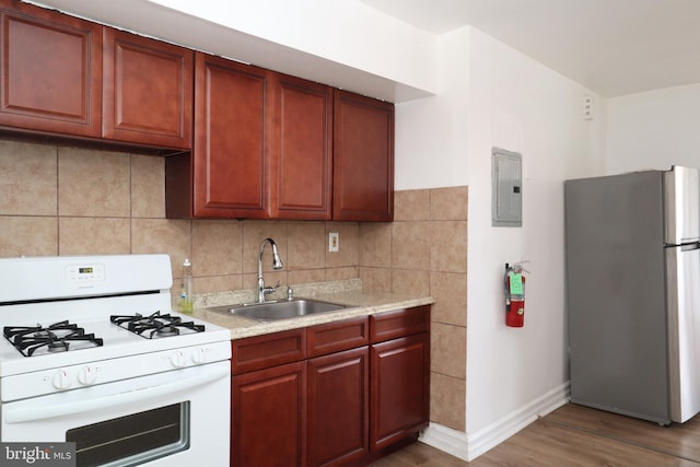 kitchen featuring electric panel, a sink, light countertops, freestanding refrigerator, and white range with gas cooktop