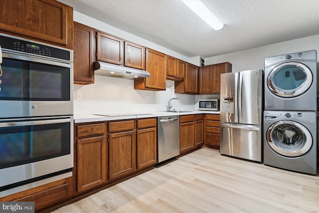 kitchen with stacked washer and dryer, light wood-type flooring, stainless steel appliances, and sink