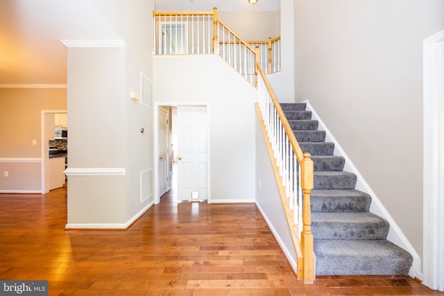 stairway featuring wood-type flooring, crown molding, and a towering ceiling