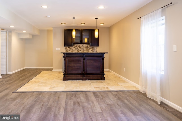 bar with dark brown cabinetry, backsplash, hanging light fixtures, and light hardwood / wood-style floors