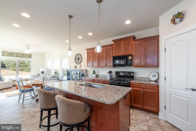 kitchen with an island with sink, sink, black appliances, pendant lighting, and ceiling fan