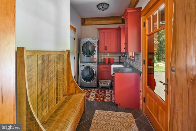 clothes washing area featuring stacked washer and dryer, dark tile patterned flooring, sink, and cabinets