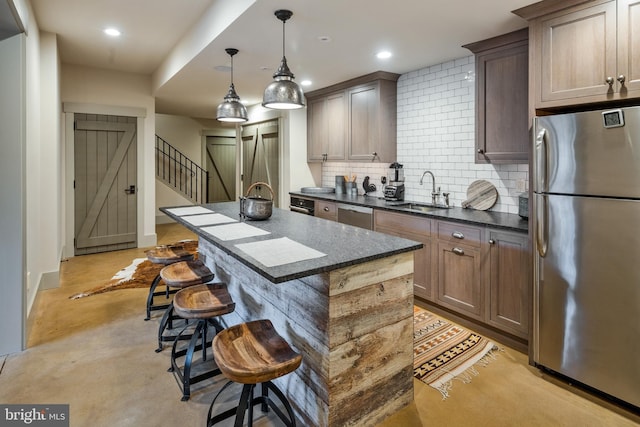 kitchen featuring decorative backsplash, a kitchen island with sink, decorative light fixtures, sink, and stainless steel appliances