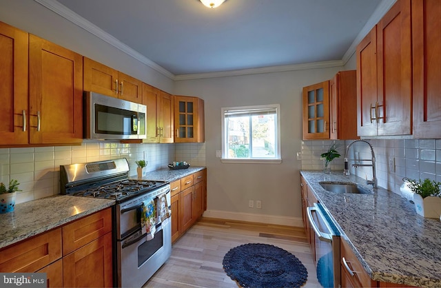 kitchen with decorative backsplash, light wood-type flooring, crown molding, stainless steel appliances, and light stone countertops