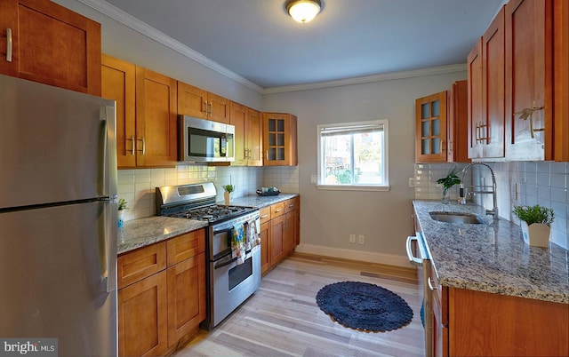 kitchen with light wood-type flooring, light stone counters, stainless steel appliances, tasteful backsplash, and sink