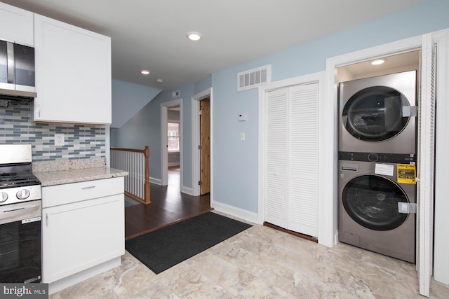 kitchen featuring stove, light stone countertops, decorative backsplash, white cabinets, and stacked washer and dryer