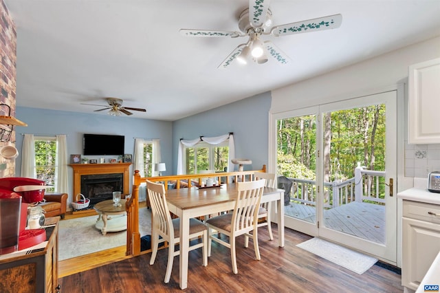 dining room featuring a large fireplace, ceiling fan, dark hardwood / wood-style floors, and a healthy amount of sunlight