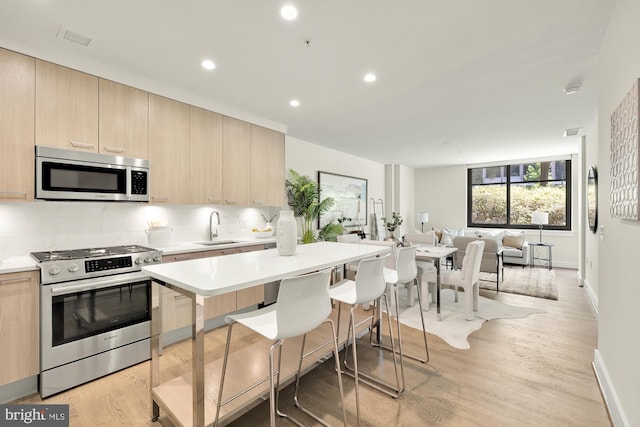 kitchen with light wood-type flooring, tasteful backsplash, sink, a breakfast bar area, and appliances with stainless steel finishes