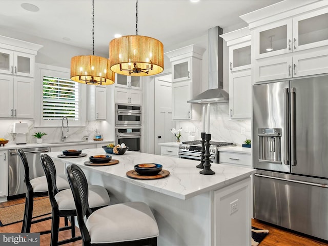 kitchen featuring wall chimney exhaust hood, white cabinets, premium appliances, and a kitchen island