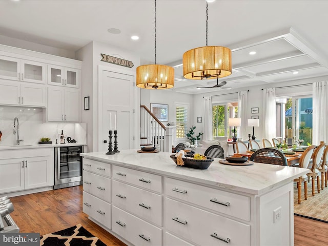 kitchen featuring white cabinets, wine cooler, sink, a kitchen island, and light wood-type flooring