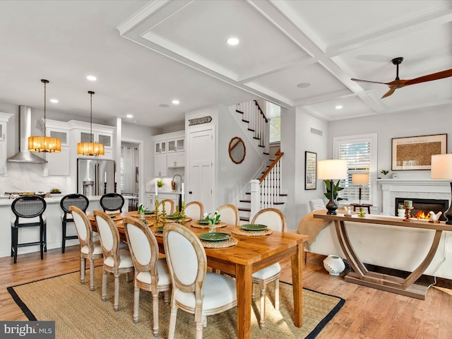 dining space with beam ceiling, coffered ceiling, ceiling fan with notable chandelier, and light hardwood / wood-style flooring