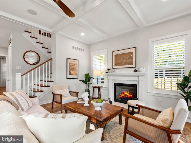 living room featuring a premium fireplace, beamed ceiling, and hardwood / wood-style flooring