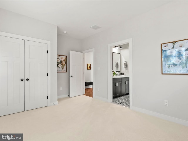 unfurnished bedroom featuring a closet, light colored carpet, and ensuite bath