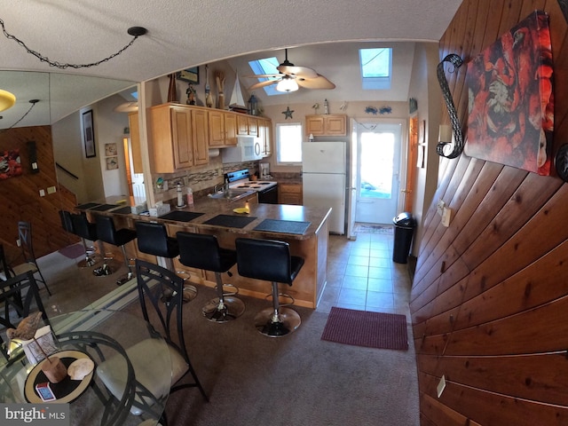 kitchen with ceiling fan, white appliances, wooden walls, kitchen peninsula, and a textured ceiling