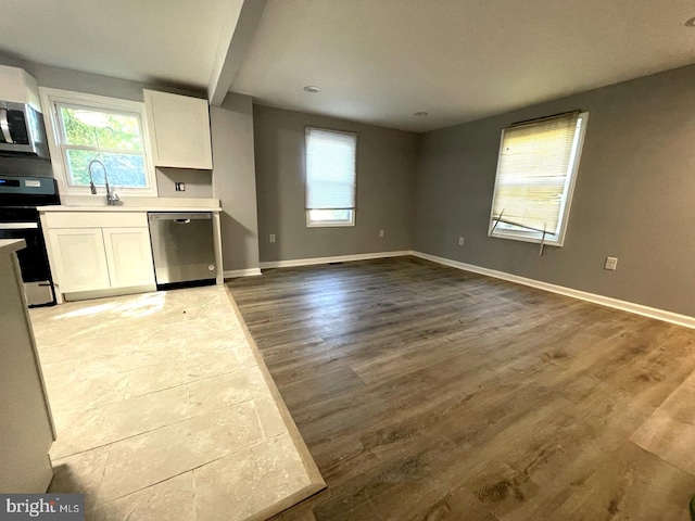 kitchen with light hardwood / wood-style floors, beamed ceiling, sink, appliances with stainless steel finishes, and white cabinetry