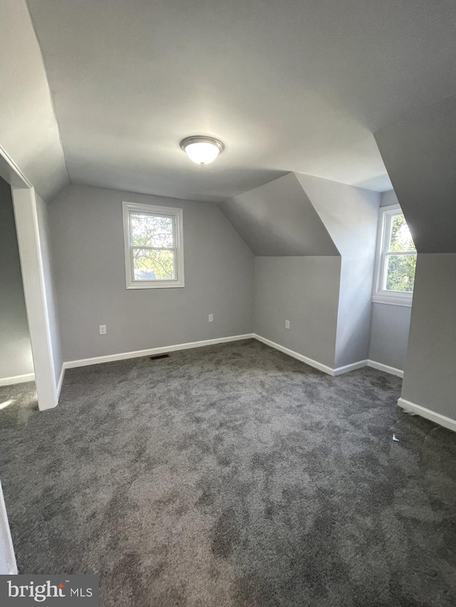 bonus room with dark colored carpet, plenty of natural light, and vaulted ceiling