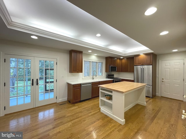 kitchen with stainless steel appliances, sink, a raised ceiling, butcher block countertops, and a kitchen island