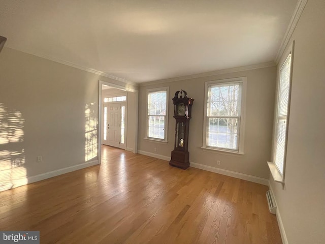 interior space featuring baseboard heating, light wood-type flooring, and crown molding