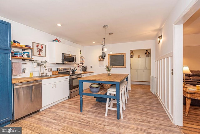 kitchen featuring white cabinetry, sink, pendant lighting, light hardwood / wood-style floors, and stainless steel appliances