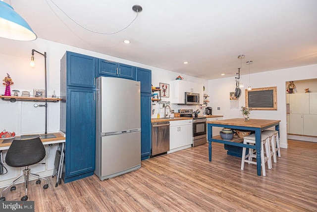 kitchen featuring hanging light fixtures, sink, blue cabinets, appliances with stainless steel finishes, and light hardwood / wood-style floors