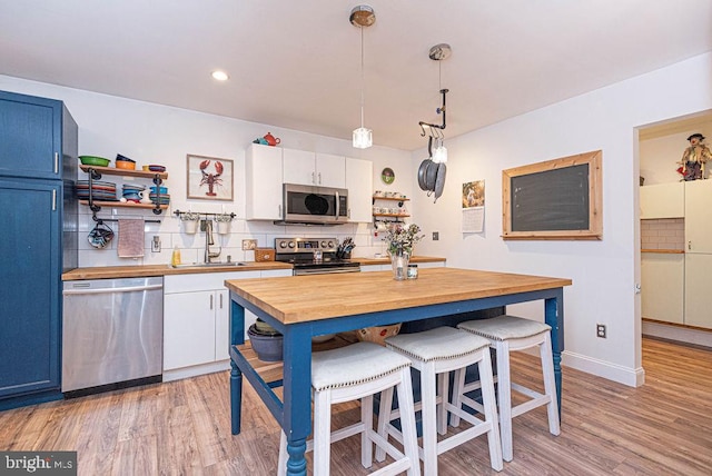 kitchen featuring appliances with stainless steel finishes, backsplash, blue cabinets, hanging light fixtures, and white cabinetry