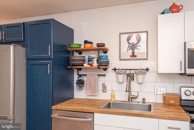 kitchen with butcher block counters, stainless steel appliances, backsplash, sink, and blue cabinets