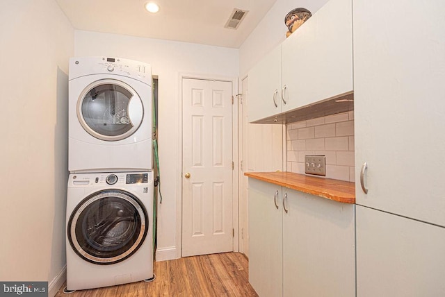 laundry room featuring cabinets, stacked washer / drying machine, and light wood-type flooring