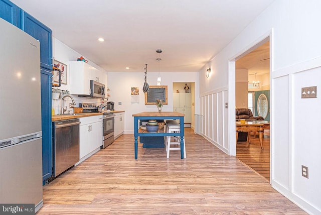 kitchen with white cabinets, light wood-type flooring, stainless steel appliances, pendant lighting, and blue cabinets