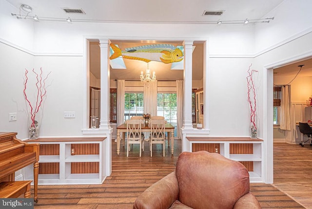 living room featuring an inviting chandelier, ornate columns, hardwood / wood-style flooring, and rail lighting