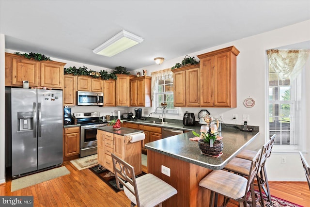 kitchen featuring a kitchen island, light hardwood / wood-style flooring, stainless steel appliances, sink, and a breakfast bar