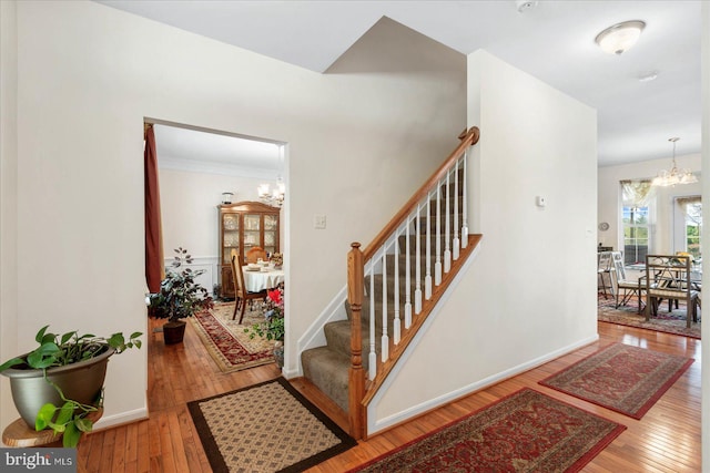 stairs with crown molding, wood-type flooring, and an inviting chandelier