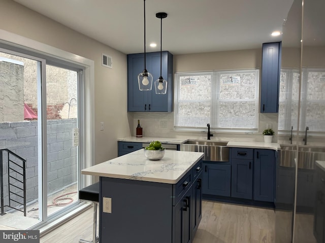 kitchen featuring a center island, blue cabinetry, decorative light fixtures, sink, and light hardwood / wood-style flooring