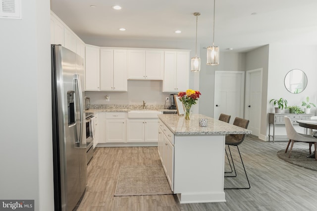 kitchen featuring white cabinets, light hardwood / wood-style floors, hanging light fixtures, appliances with stainless steel finishes, and a kitchen breakfast bar