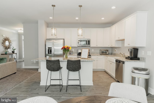 kitchen featuring stainless steel appliances, hanging light fixtures, a center island, and white cabinetry