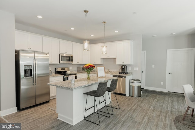 kitchen featuring white cabinets, hanging light fixtures, stainless steel appliances, a center island, and light hardwood / wood-style floors