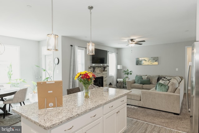 kitchen with hanging light fixtures, a stone fireplace, white cabinetry, a center island, and light wood-type flooring