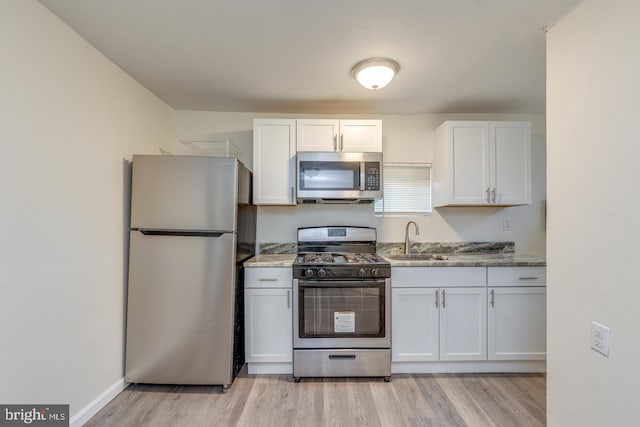 kitchen with white cabinetry, sink, stainless steel appliances, and light stone counters