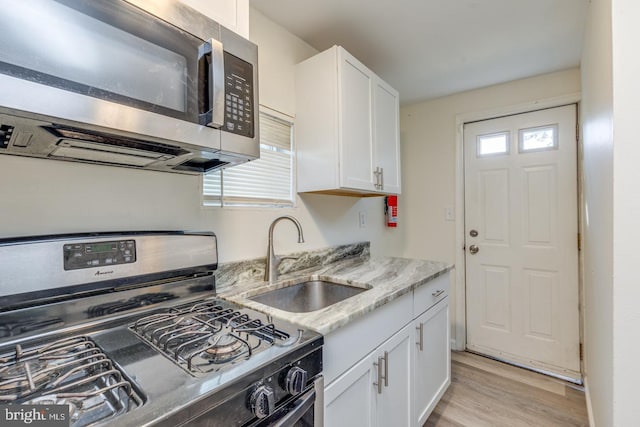 kitchen featuring sink, light hardwood / wood-style flooring, light stone countertops, white cabinetry, and range with gas cooktop