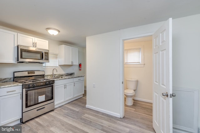 kitchen featuring appliances with stainless steel finishes, light wood-type flooring, white cabinetry, and light stone counters