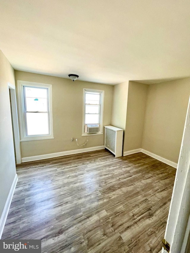 spare room featuring radiator, wood-type flooring, cooling unit, and plenty of natural light