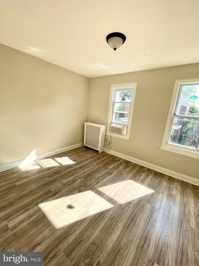 empty room with cooling unit, radiator heating unit, and hardwood / wood-style floors