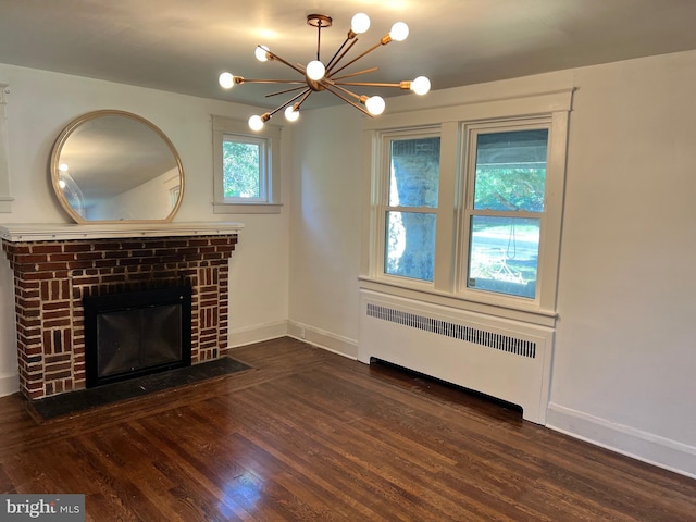 unfurnished living room with radiator, a notable chandelier, dark wood-type flooring, and a brick fireplace