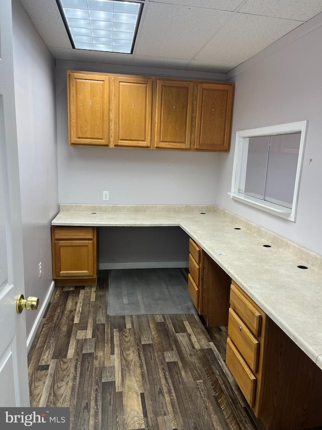 unfurnished office featuring a drop ceiling, dark hardwood / wood-style floors, and built in desk