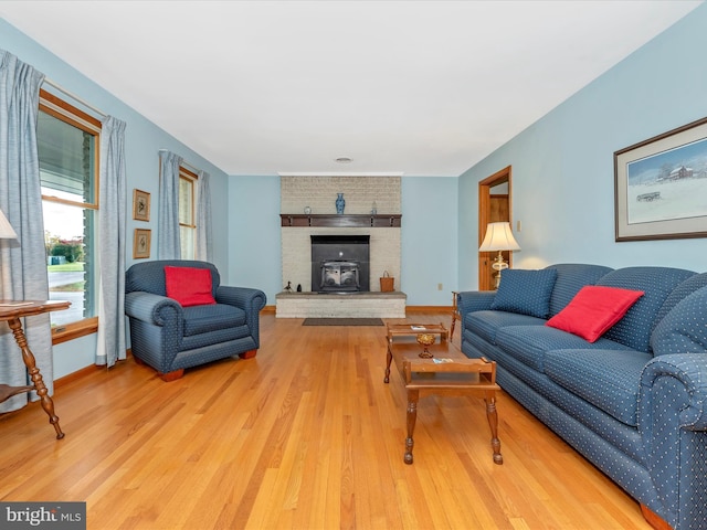 living area with a brick fireplace, light wood-type flooring, and baseboards