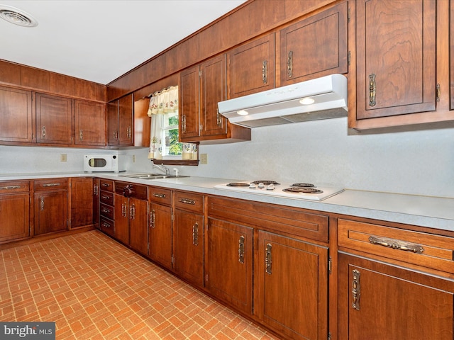 kitchen featuring white appliances, brick patterned floor, under cabinet range hood, light countertops, and a sink